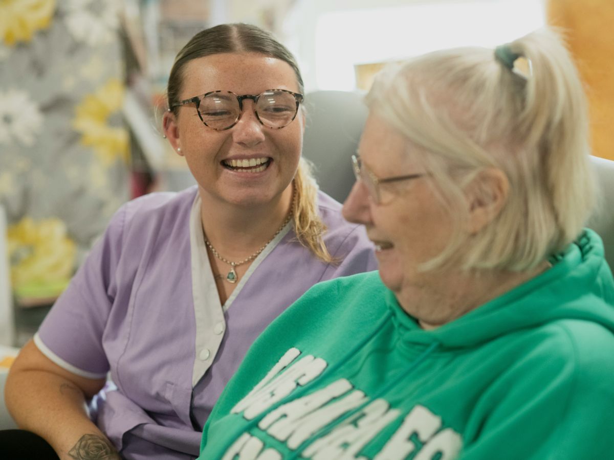 A smiling caregiver sharing a laugh with an older woman at home